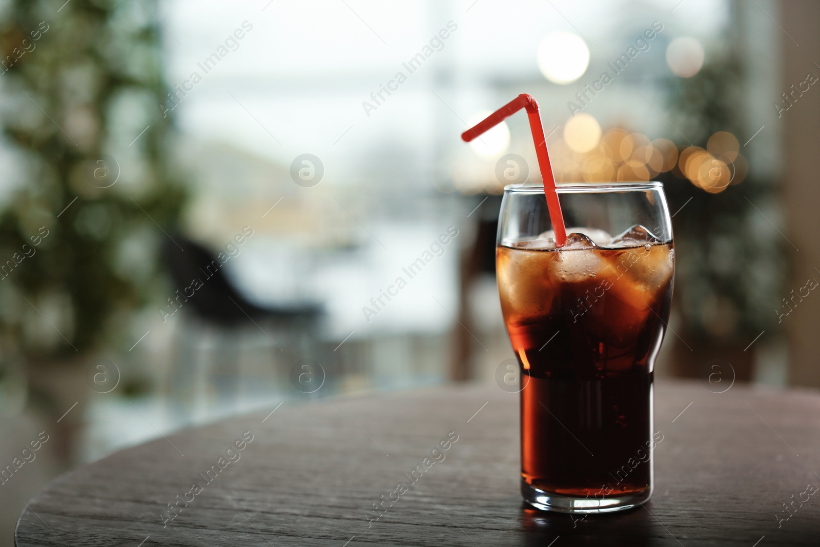 Photo of Glass of cold cola on table against blurred background. Space for text