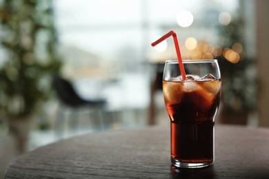 Photo of Glass of cold cola on table against blurred background. Space for text