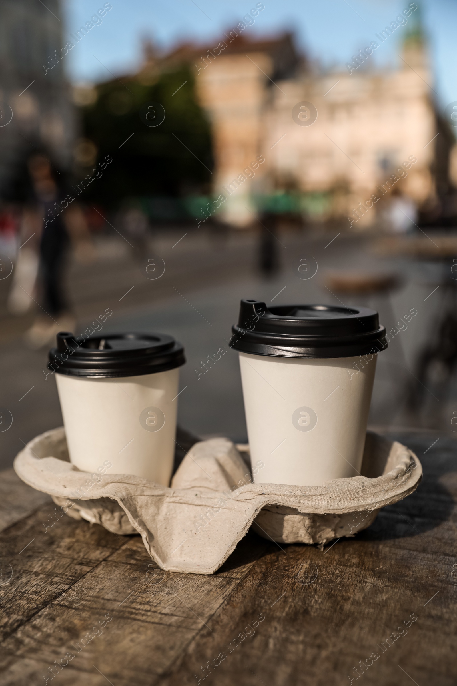 Photo of Cardboard takeaway coffee cups with plastic lids and holder on wooden table in city