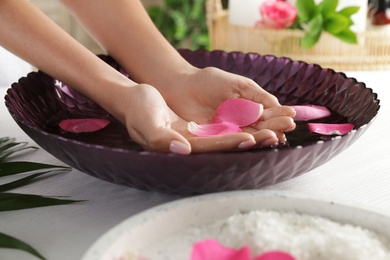 Woman soaking her hands in bowl with water and petals on table, closeup. Spa treatment
