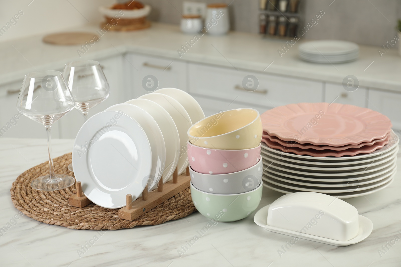 Photo of Clean plates, bowls, butter dish and glasses on white marble table in kitchen