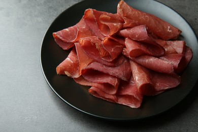 Photo of Plate with tasty bresaola on grey table, closeup