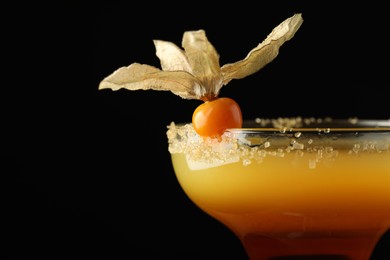 Photo of Tasty cocktail decorated with physalis fruit on black background, closeup