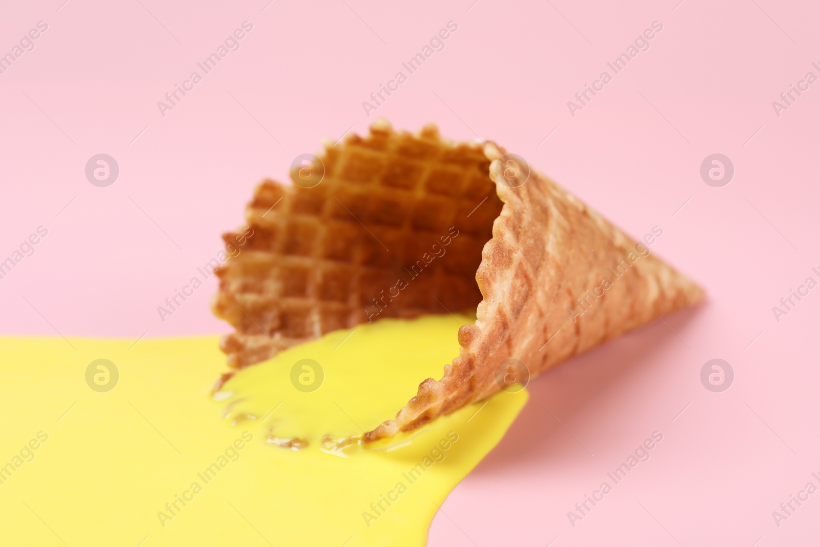 Photo of Melted ice cream and wafer cone on pink background, closeup