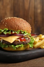 Delicious burger with beef patty and french fries on wooden table, closeup