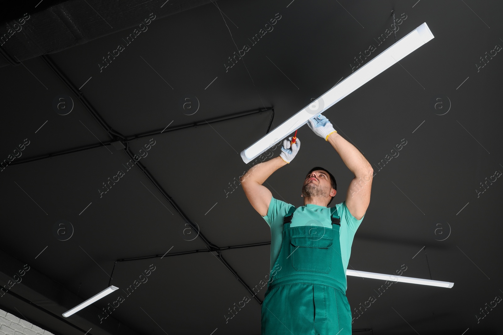 Photo of Ceiling light. Electrician installing led linear lamp indoors, low angle view. Space for text