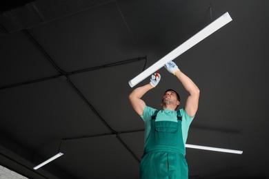 Photo of Ceiling light. Electrician installing led linear lamp indoors, low angle view. Space for text