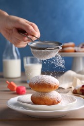Photo of Woman dusting powdered sugar onto delicious Hanukkah donuts on wooden table, closeup