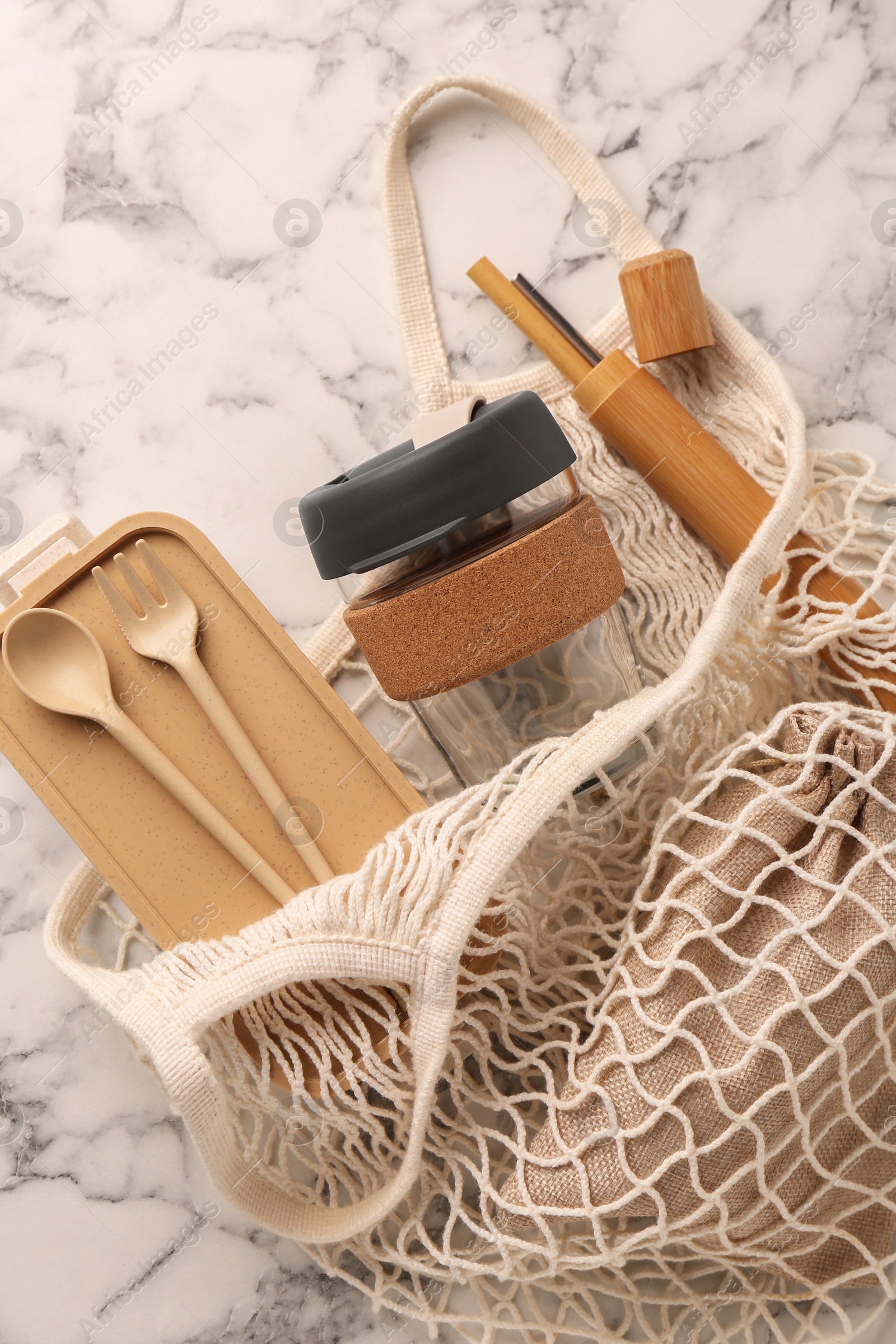 Photo of Net bag with different items on white marble table, top view. Conscious consumption