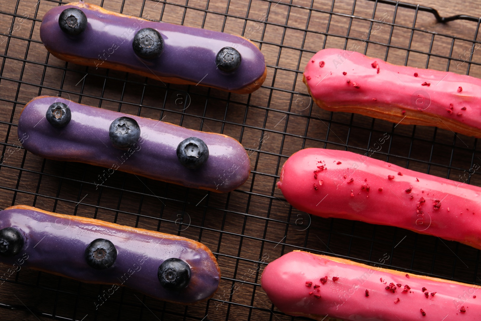 Photo of Cooling rack with different tasty glazed eclairs on wooden table, top view