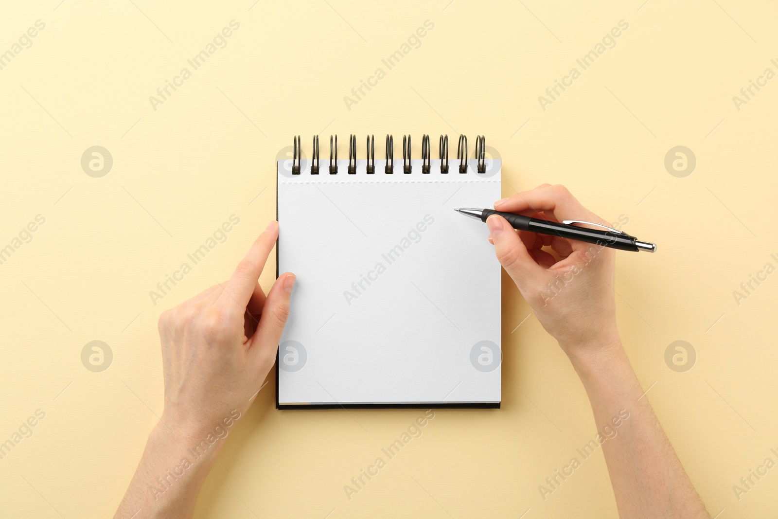 Photo of Woman writing in notebook on beige background, top view