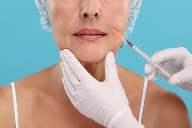 Photo of Doctor giving facial injection to senior woman on light blue background, closeup. Cosmetic surgery