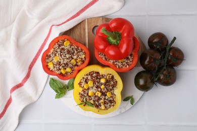 Photo of Quinoa stuffed bell peppers, tomatoes and basil on white tiled table, flat lay