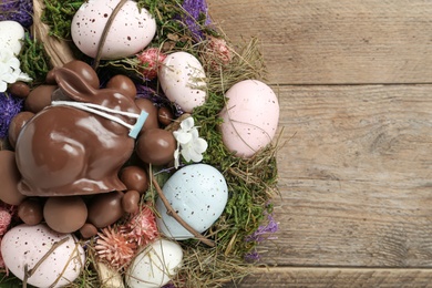 Photo of Chocolate  bunny with protective mask, eggs, wreath and space for text on wooden table, flat lay. Easter holiday during COVID-19 quarantine