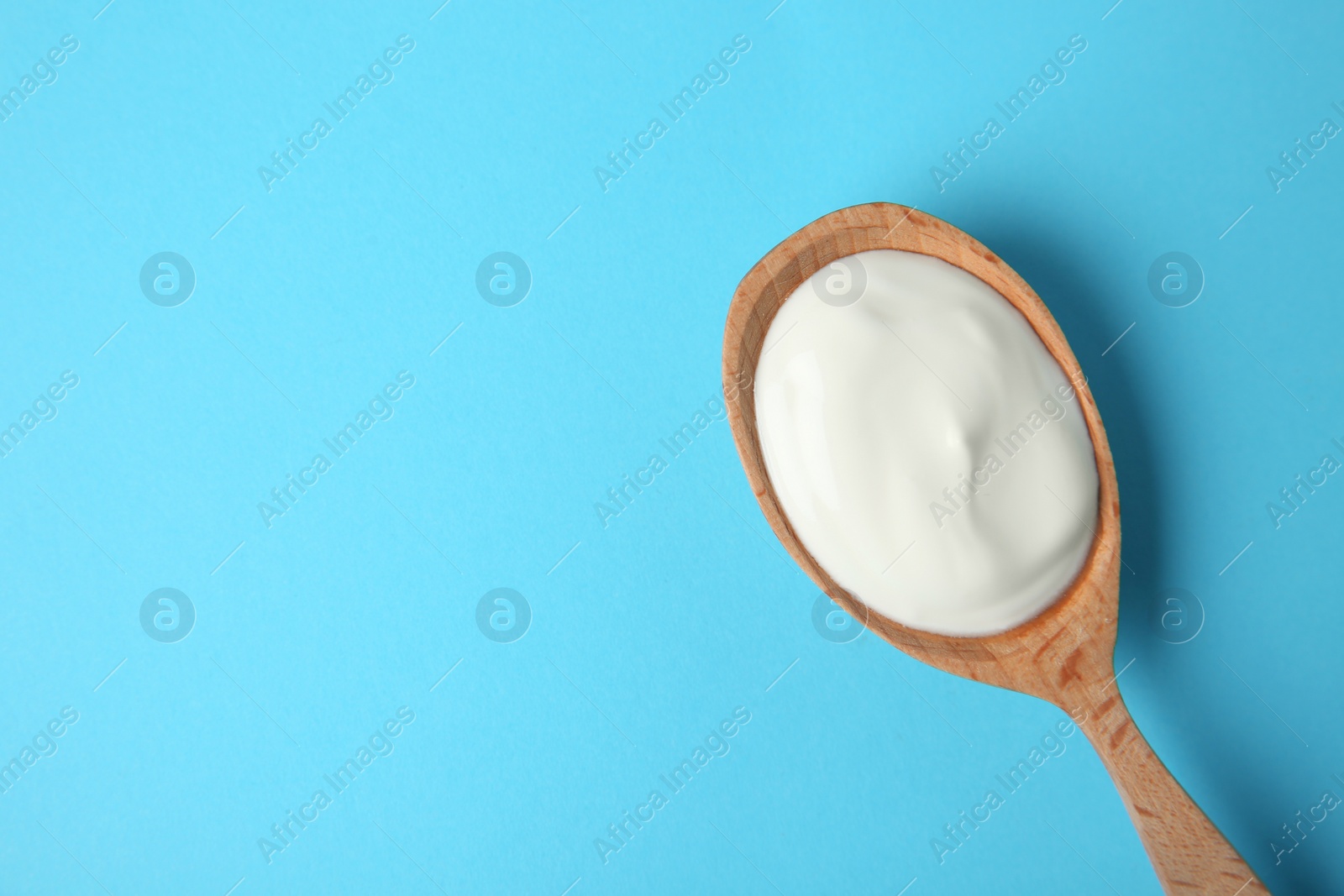 Photo of Wooden spoon of sour cream on light blue background, top view. Space for text