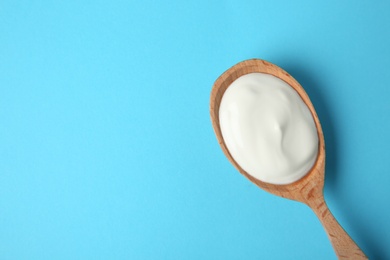 Photo of Wooden spoon of sour cream on light blue background, top view. Space for text