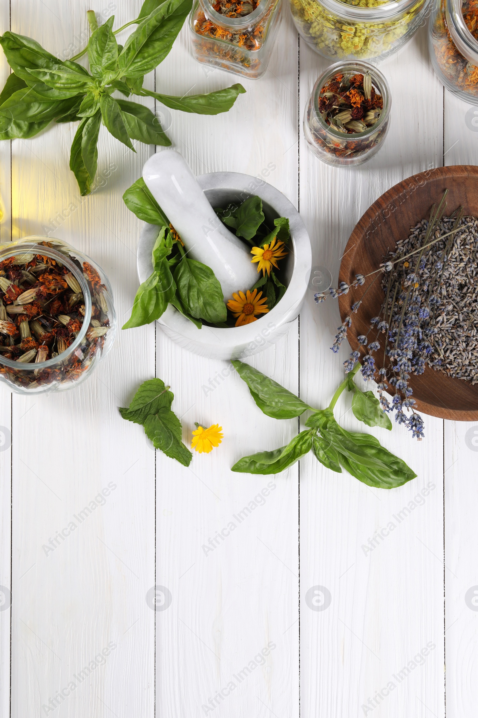 Photo of Mortar with pestle and many different herbs on white wooden table, flat lay. Space for text