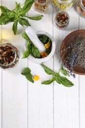 Mortar with pestle and many different herbs on white wooden table, flat lay. Space for text