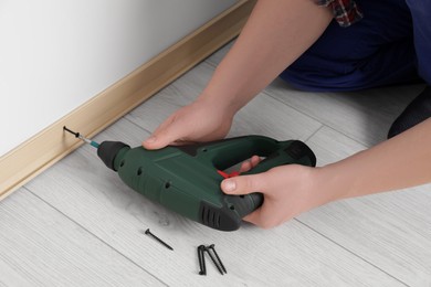 Man installing plinth on laminated floor with screwdriver in room, closeup