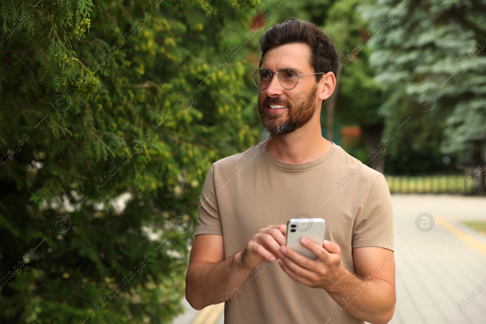 Photo of Smiling handsome bearded man with smartphone outdoors. Space for text