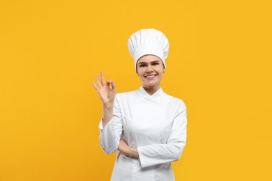 Happy female chef showing ok gesture on orange background
