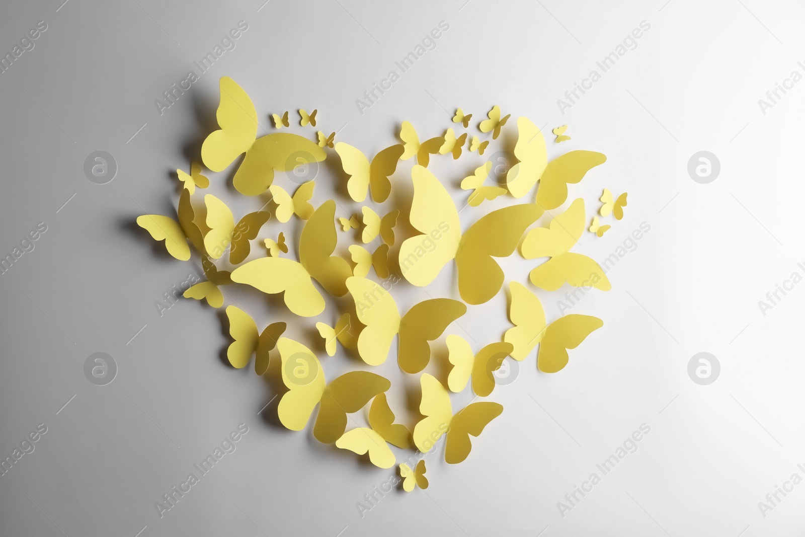 Photo of Heart shape made of yellow paper butterflies on white background, top view