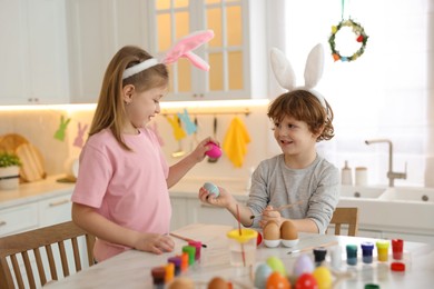 Easter celebration. Cute children with bunny ears having fun while painting eggs at white marble table in kitchen