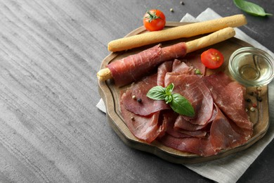 Photo of Delicious bresaola, tomato, grissini sticks and basil leaves on grey textured table. Space for text