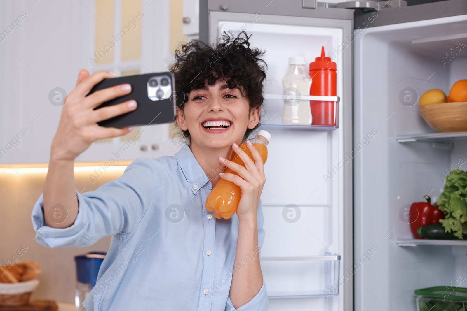 Photo of Smiling food blogger with bottle of juice taking selfie near fridge in kitchen