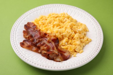 Delicious scrambled eggs with bacon in plate on light green background