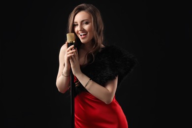 Photo of Beautiful young woman in stylish dress with microphone singing on black background