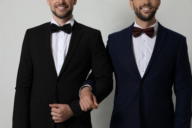 Photo of Happy gay couple in elegant suits standing near white wall, closeup