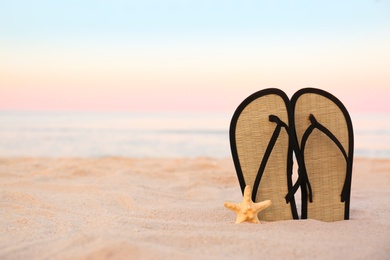 Photo of Stylish flip flops on sand near sea, space for text. Beach accessories