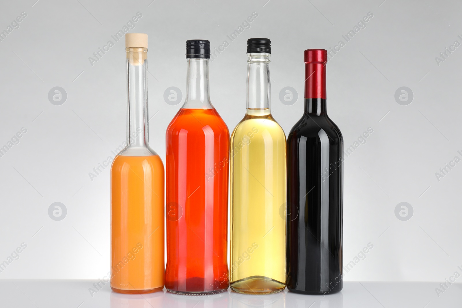 Photo of Bottles of different alcoholic drinks on white table against light background