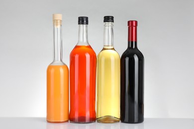 Bottles of different alcoholic drinks on white table against light background