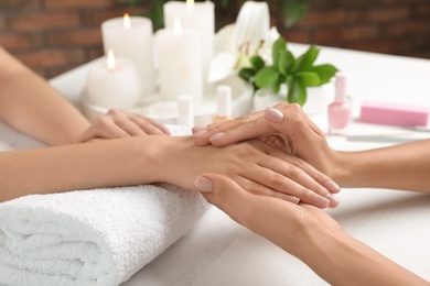 Photo of Cosmetologist massaging client's hand at table in spa salon, closeup