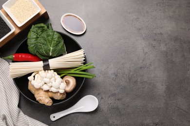 Cooking delicious ramen soup. Different ingredients in bowls and spoon on gray table, flat lay. Space for text