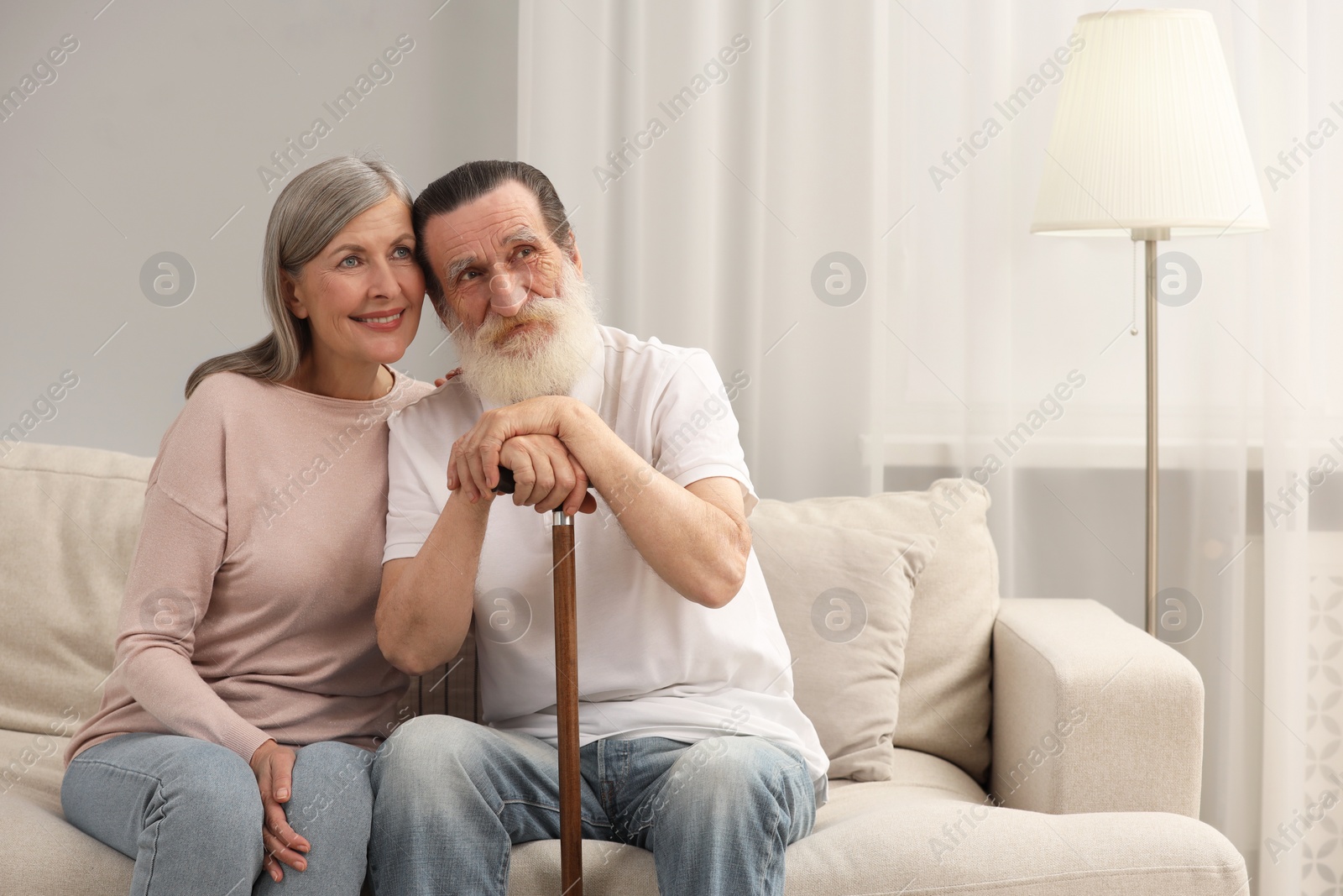 Photo of Senior man with walking cane and mature woman on sofa at home