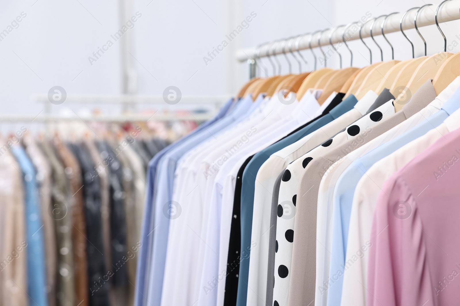 Photo of Dry-cleaning service. Many different clothes hanging on rack indoors, closeup