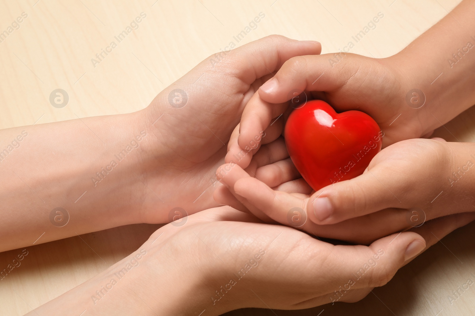 Photo of Woman and child holding heart on beige wooden background, closeup. Donation concept