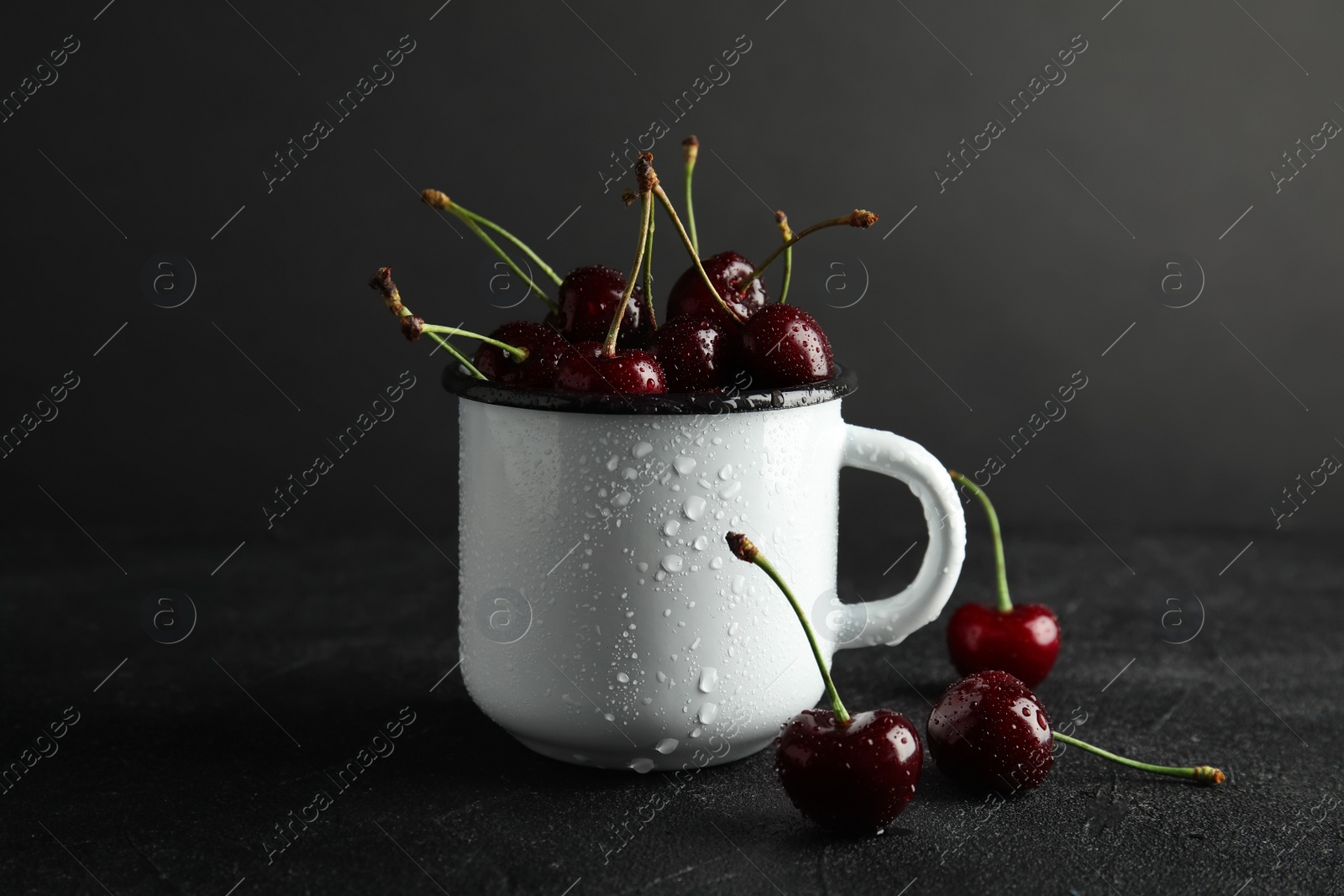 Photo of Mug with sweet red cherries on table