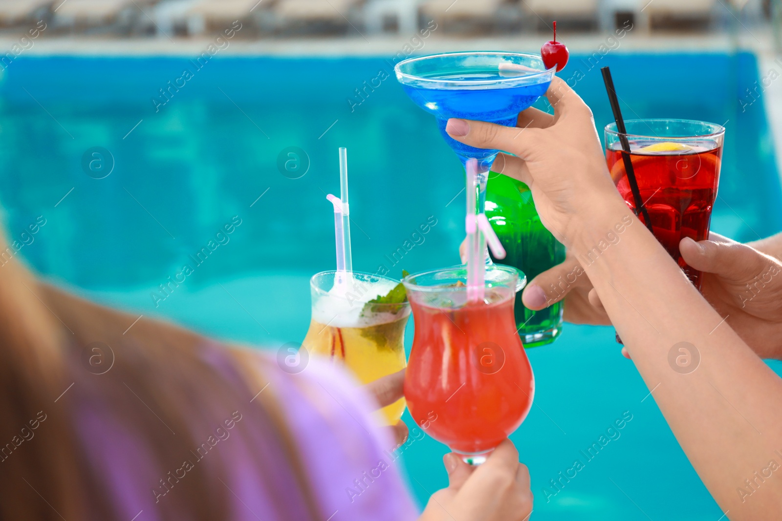 Photo of Friends clinking glasses with fresh summer cocktails near swimming pool, closeup