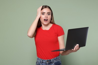 Emotional woman with laptop on pale green background