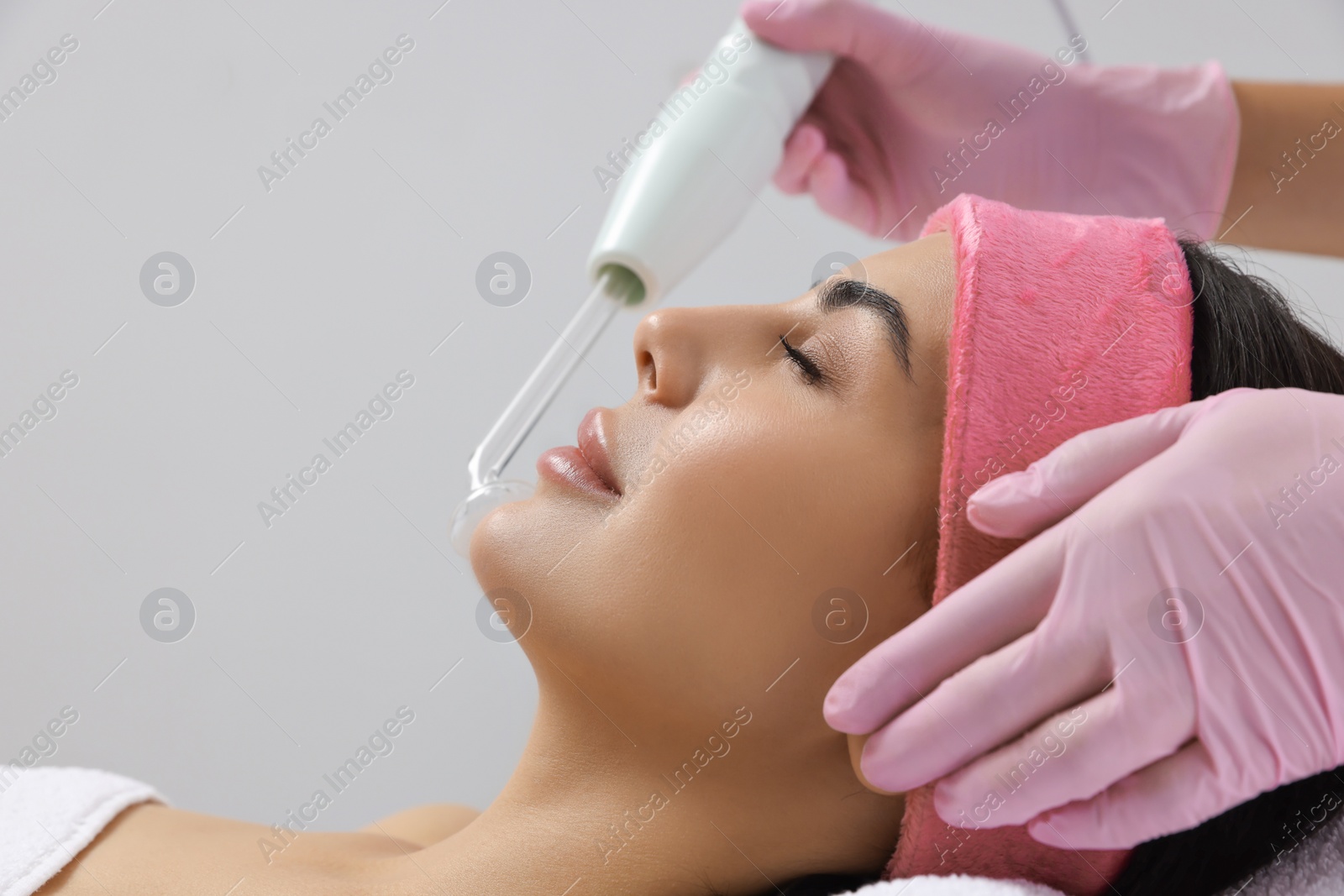 Photo of Young woman undergoing face rejuvenation procedure with darsonval in salon, closeup