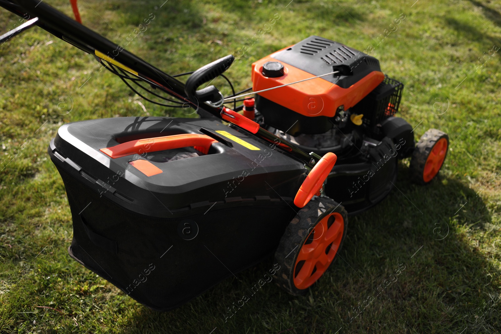 Photo of Modern lawn mower on green grass outdoors
