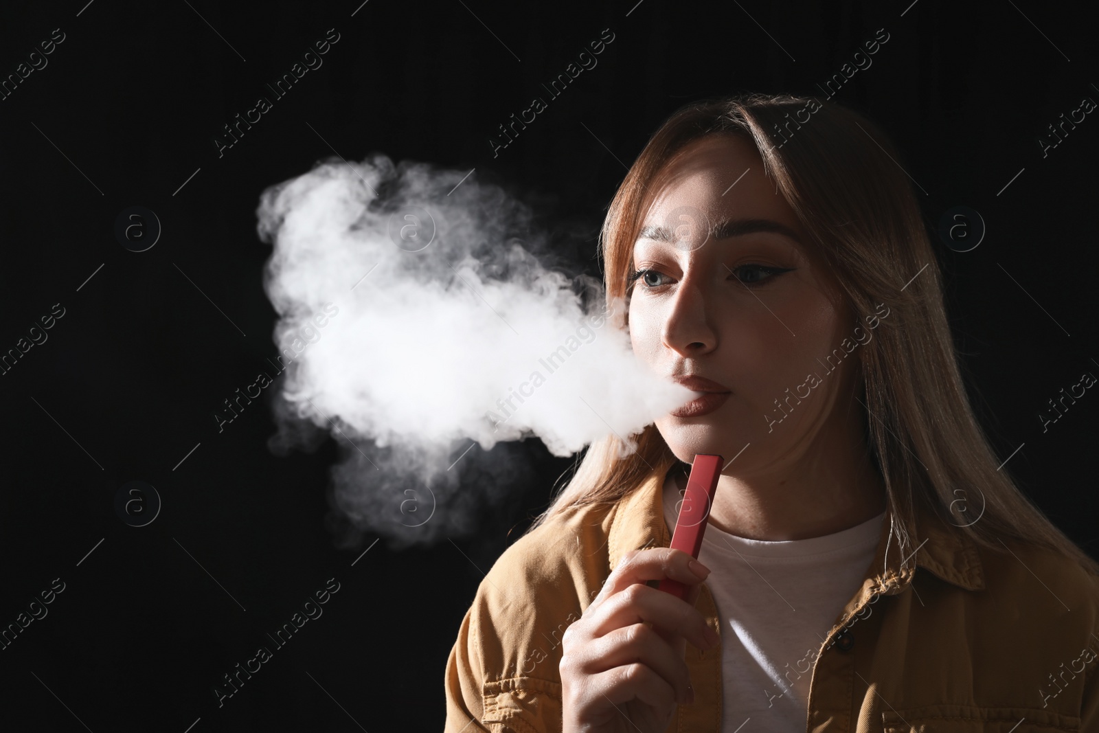 Photo of Young woman using electronic cigarette on black background