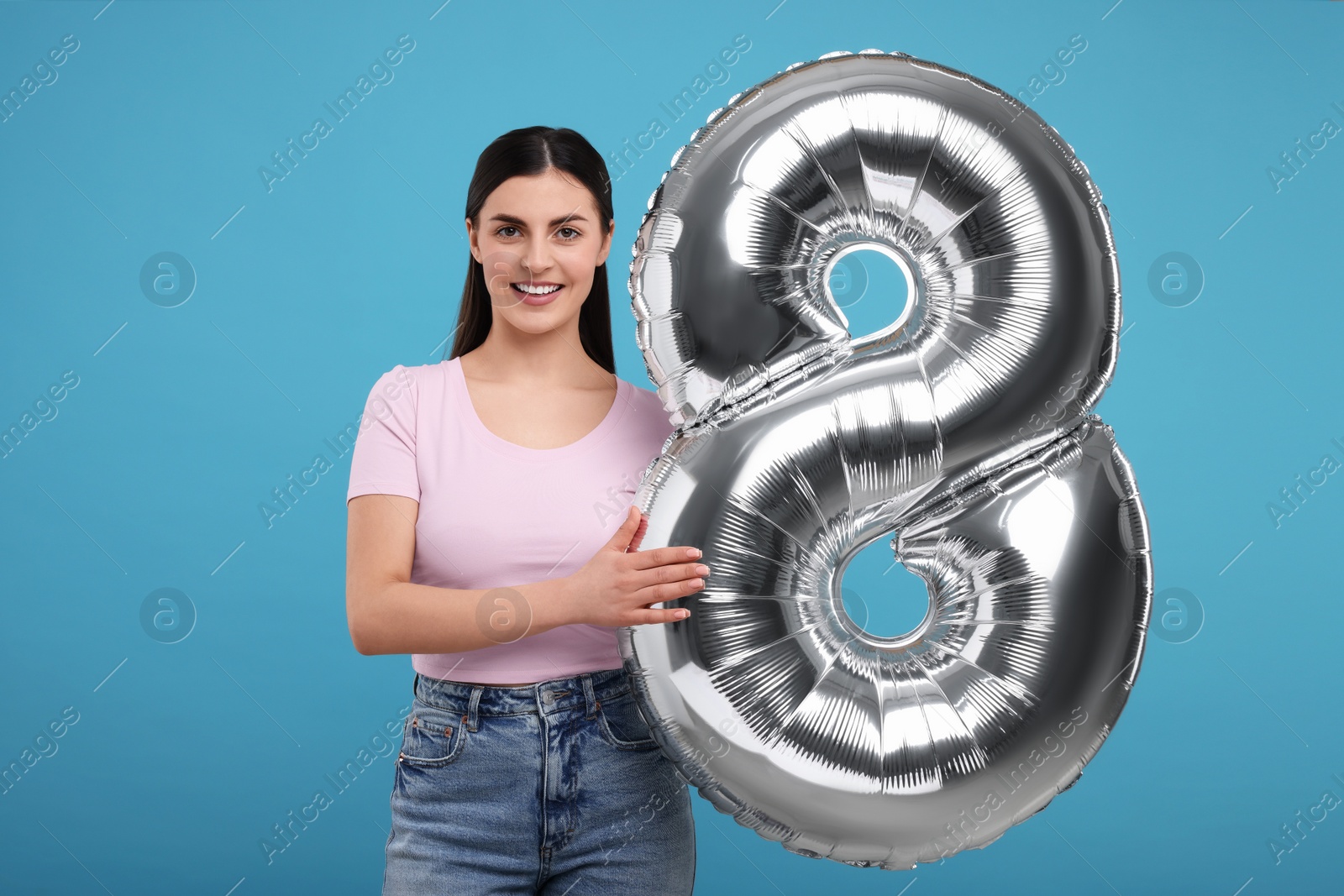 Photo of Happy Women's Day. Charming lady holding balloon in shape of number 8 on light blue background