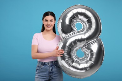 Happy Women's Day. Charming lady holding balloon in shape of number 8 on light blue background