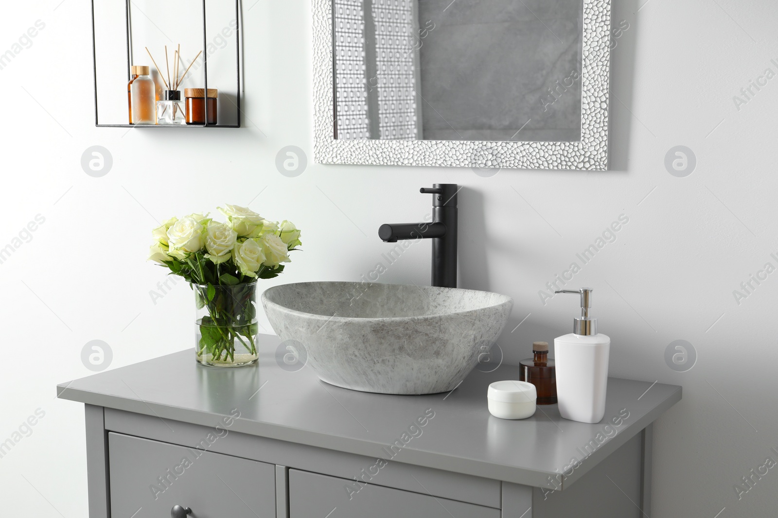 Photo of Vase with beautiful white roses and toiletries near sink in bathroom