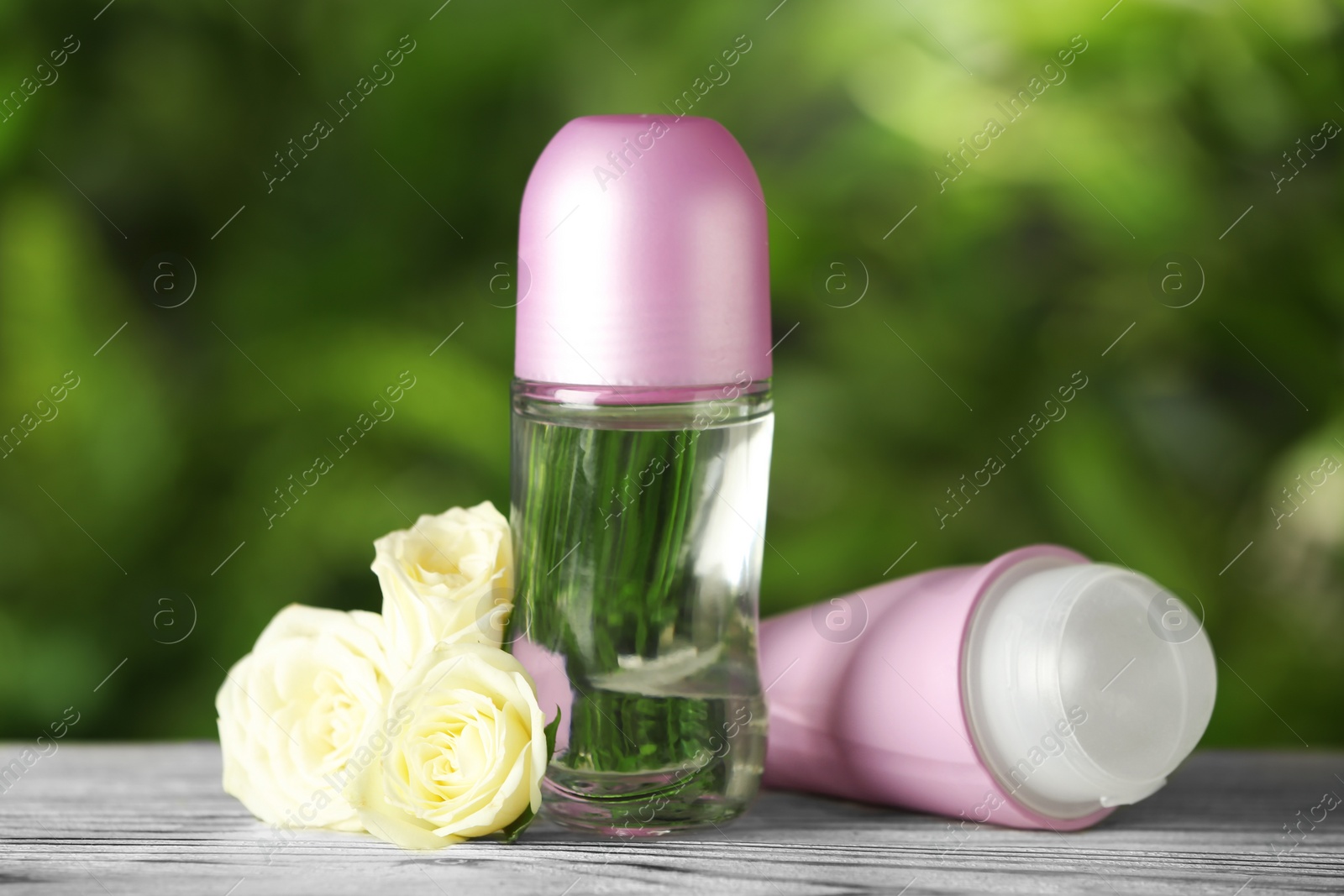 Photo of Natural deodorants with white roses on wooden table against blurred green background